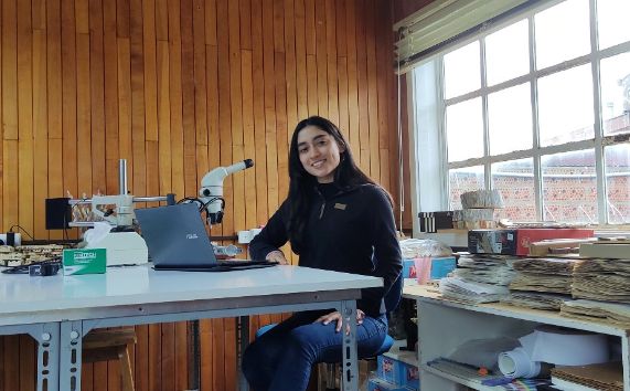 Estudiante de Geografía UChile, Milca Pizarro, posando junto a un microscopio en el centro de investigación GAIA Antártica de la U. de Magallanes.
